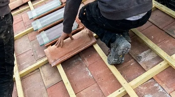 Pose d'une tuile canal sur des liteaux neufs lors d'une réfection de toiture à Aubagne